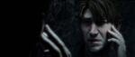 James Sunderland from the Silent Hill 2 Remake gazes into the mirror while torturously touching his own face.