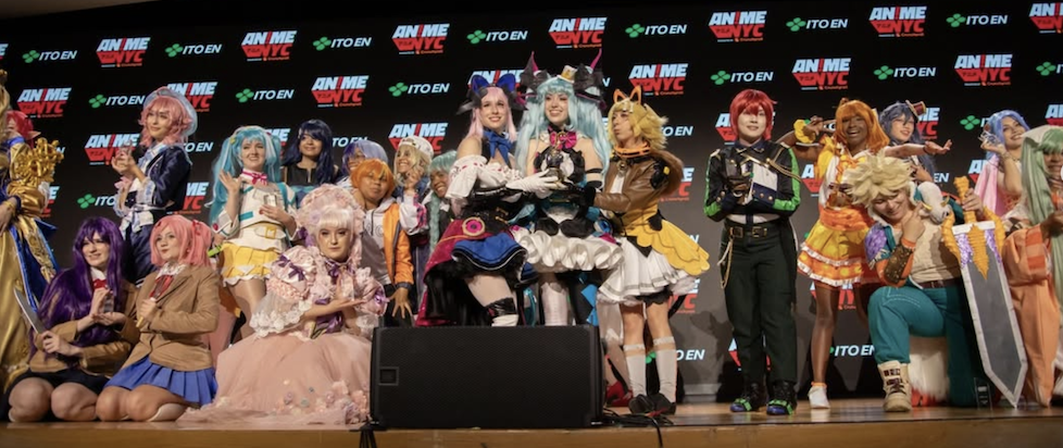 A photo from the cosplay contest at Anime NYC 2025 with lots of colorful wigs, intricate dresses, some foam weapons, animal ears, all sorts of great stuff
