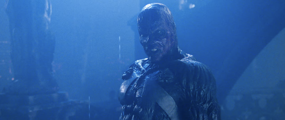 A screenshot from the trailer for Spawn where Spawn is standing looking angry with his mask off and skin all melted and everything looks blue and foggy in that 90s way
