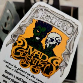 A cemetery card from Sepulchre featuring art of the mad scientist, a ghoulishly green figure holding a human skull aloft.