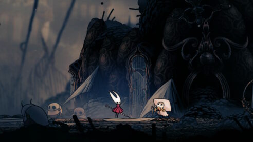 A screenshot from HOllow Knight ilksong where red mantled Hornet stands at a gate with surrounded by pilgrims