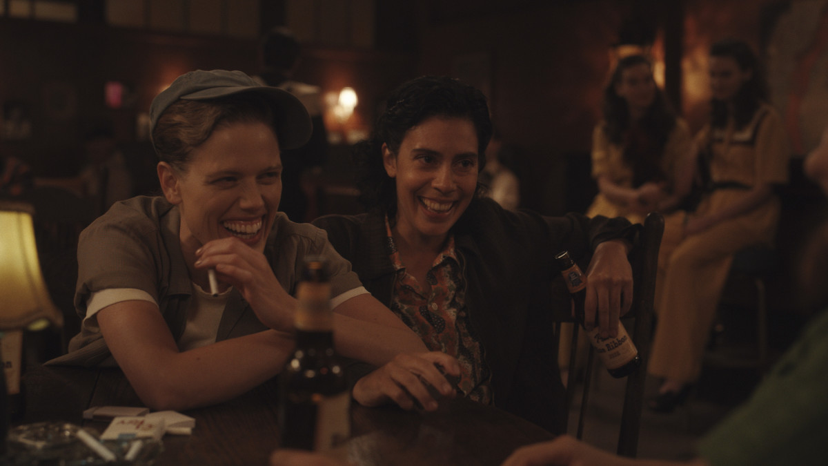 A scene from A League of Their Own shows two players laughing together in a bar.