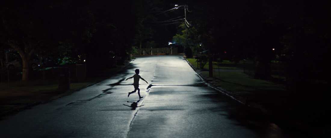 Another still from Weapons shows a child running across a moonlit street, arms splayed outwards like an airplane.