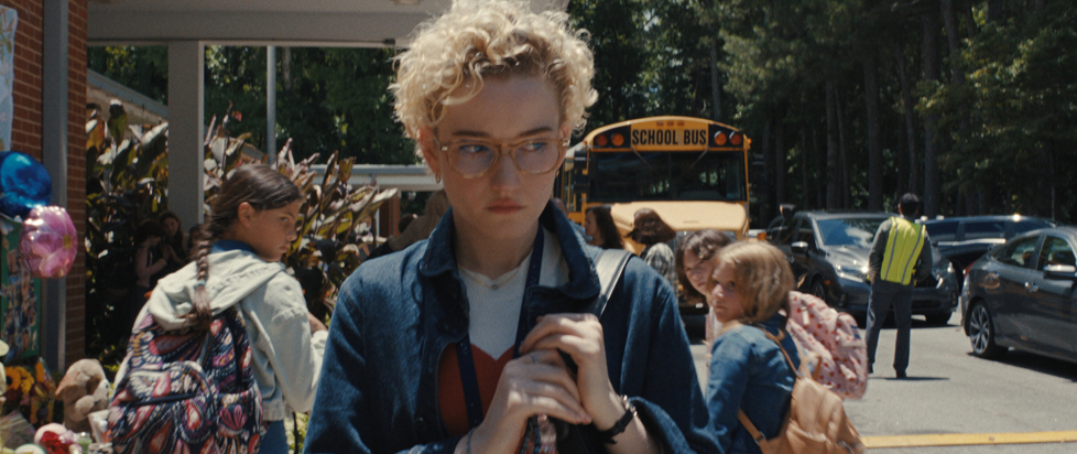 A still from Weapons shows main character Justine walking nervously through a school parking lot.