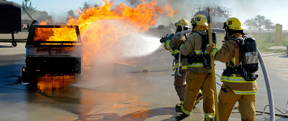 Two firefighters try to extinguish a fire in a controlled parking lot environment.