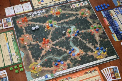 A picture of the core Root game, a board with the woods flooded with meeples and dice, and cards and meeples and various faction pages all around the sides