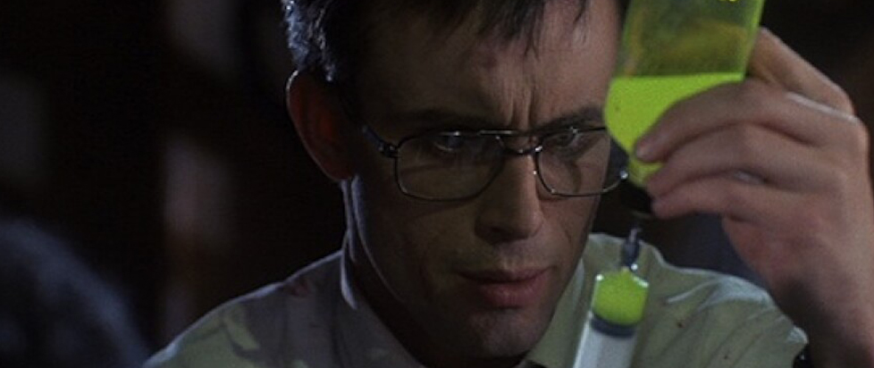 A man pulls a syringe full of glowing yellow liquid from a bottle in a scene from Re-Animator.