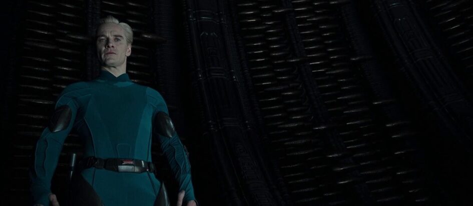 A screenshot of Alien Covenant where Blond David in a blue little uniform is looking down disdainfully at us, the viewer