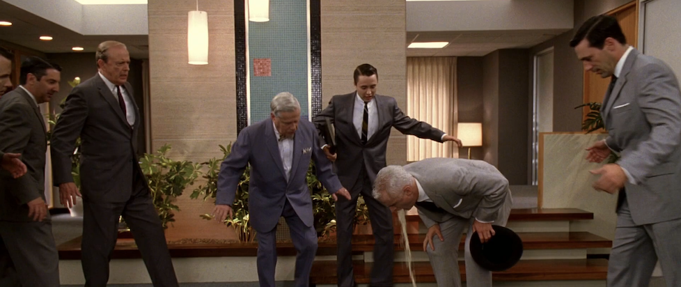 A screenshot from Mad Men season 1 episode 7 where Roger is puking his guts out and several sharp dressed men around him are trying to avoid the splash zone