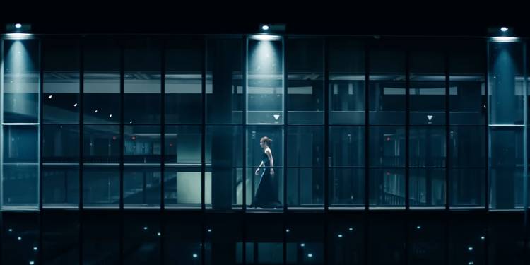 Helena is framed and spotlit by the huge glass windows at the Lumon corporate offices, appearing as a small yet significant part of a whole.