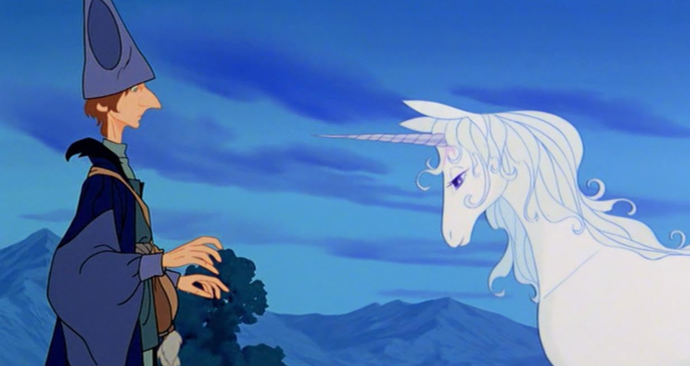 A man dressed in blue wizard's robes faces an elegant white unicorn in this still from The Last Unicorn.