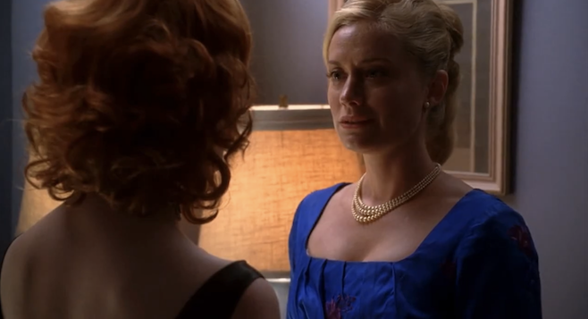 A screenshot from Mad Men where Joan's roommate in blue is confessing her love and it's showing on the roommate's face