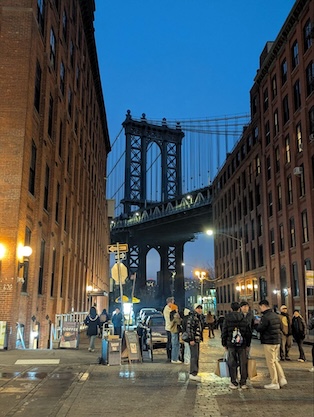 A photograph of the Manhattan Bridge just after sunset with the city lights blazing and the sky a deep blue