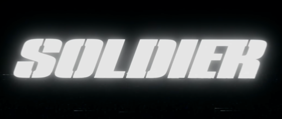 A screenshot from the trailer for the movie Soldier with the title in a bold white italic typeface on black
