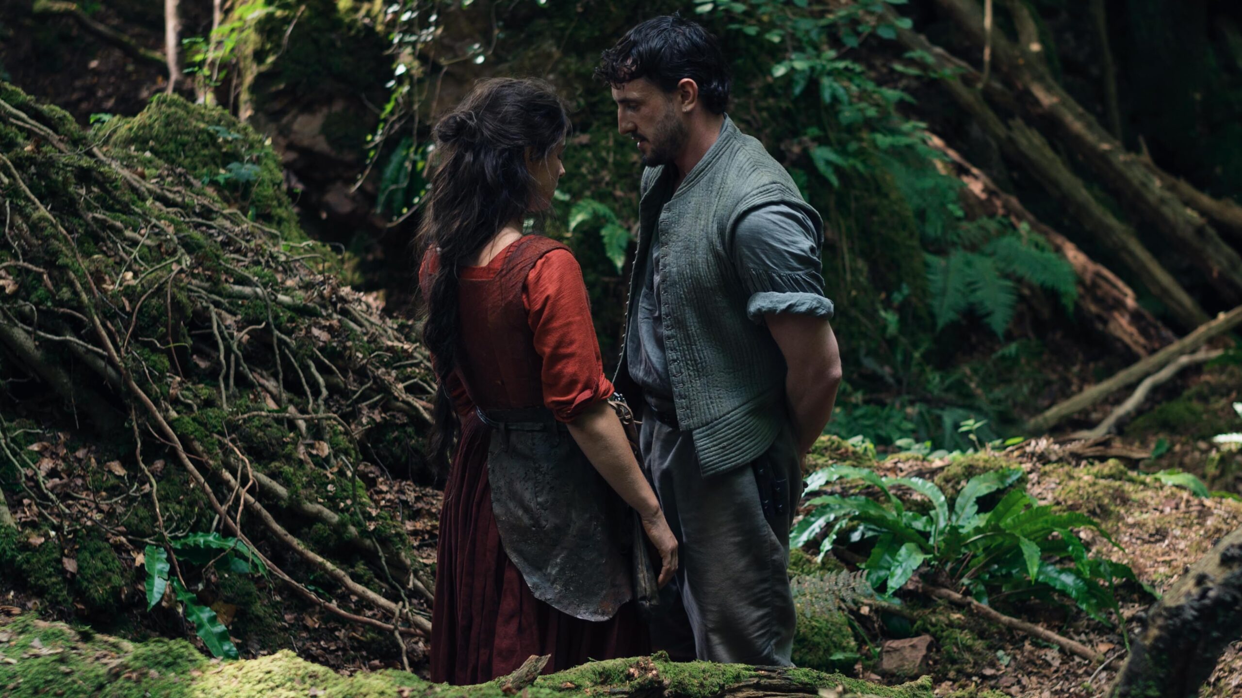 Agnes and Will Shakespeare stand very close together in a lush forest in this scene from Hamnet.