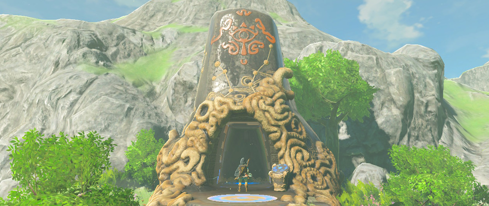 Link stands at the entrance to a Sheikah shrine, which stands next to a rocky cliff face.