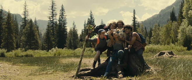 A screenshot from Bigsby Bear where a group of young people are taking a group photo while hiking in the woods all gathered in the center as friends and holding the head of Bigsby Bear