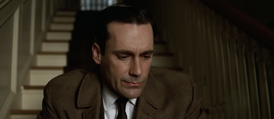 A screenshot from the finale of season 1 of Mad Men where Don is in a coat sitting on some stairs looking kinda sad