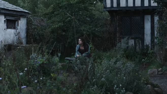 An image from Hamnet where William's wife Agnes is sitting in an overgrown yard by herself as the light dims