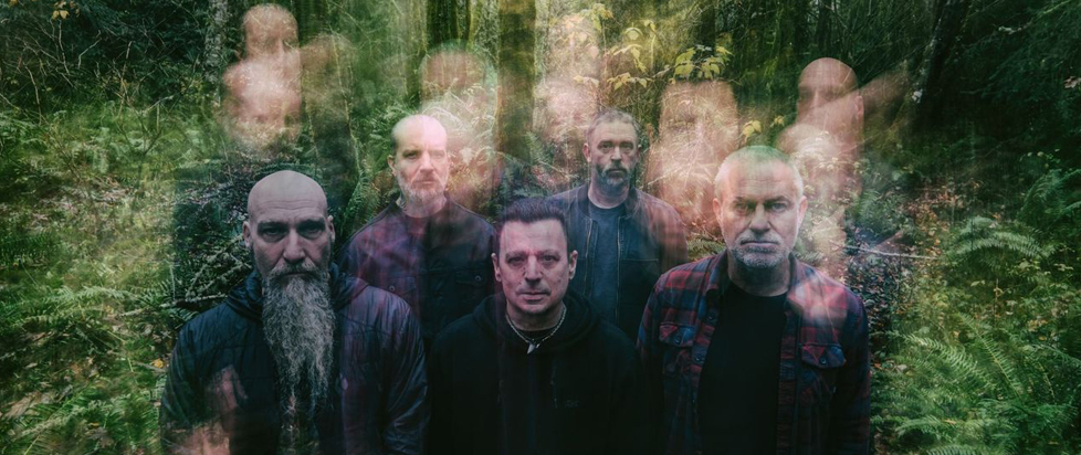 The band Neurosis poses together in the woods. A camera effect makes several of their faces appear blurred as if in motion.