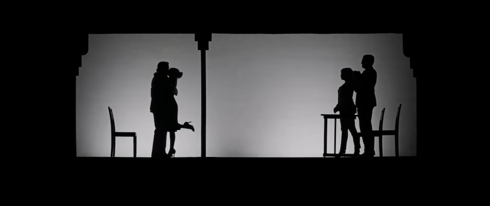 A screenshot from the trailer for La La Land with a scene from a theater in black and white silhouette with two characters kissing on the left and two others looking on the right