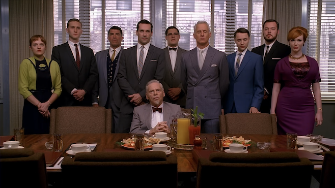 A screenshot from Mad Men where everyone in the office is standing behind one of the partners in a last supper family photo way