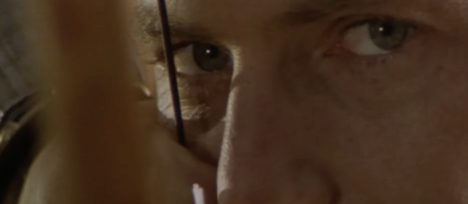 A screenshot from the trailer of Robin Hood Prince of Thieves with a very extreme closeup of Kevin Costner's dreamy eyes as he pulls a bowstring to his cheek